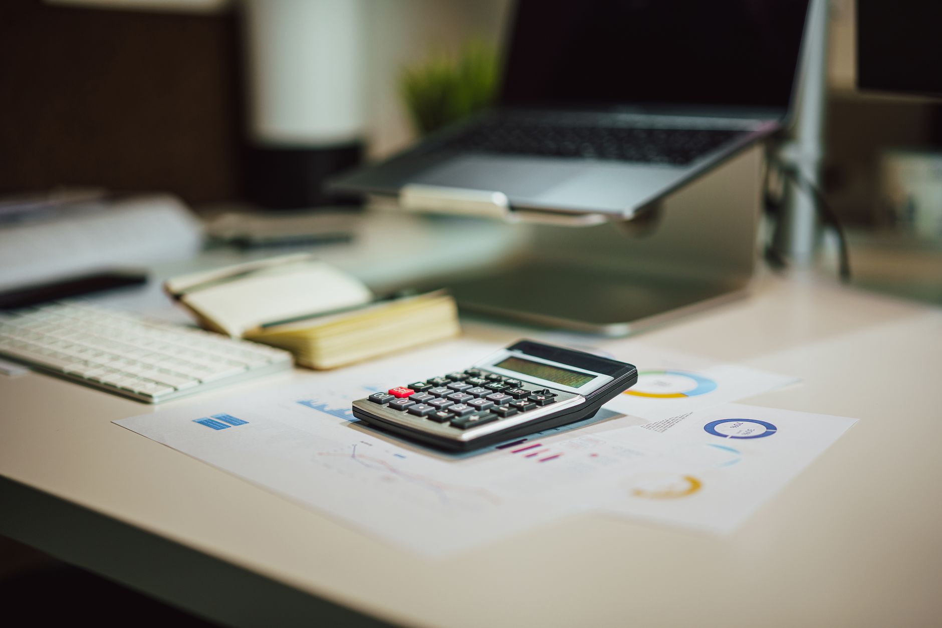 Laptop, Taschenrechner und Unterlagen auf modernem Schreibtisch für Finanzaufgaben