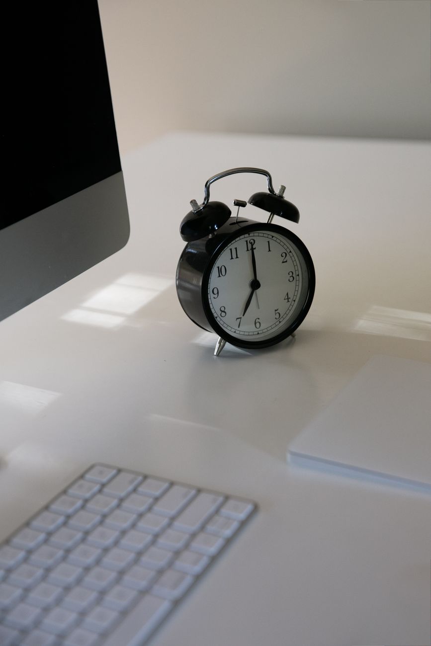Schwarzer Wecker steht neben Tastatur und Computer auf einem Schreibtisch