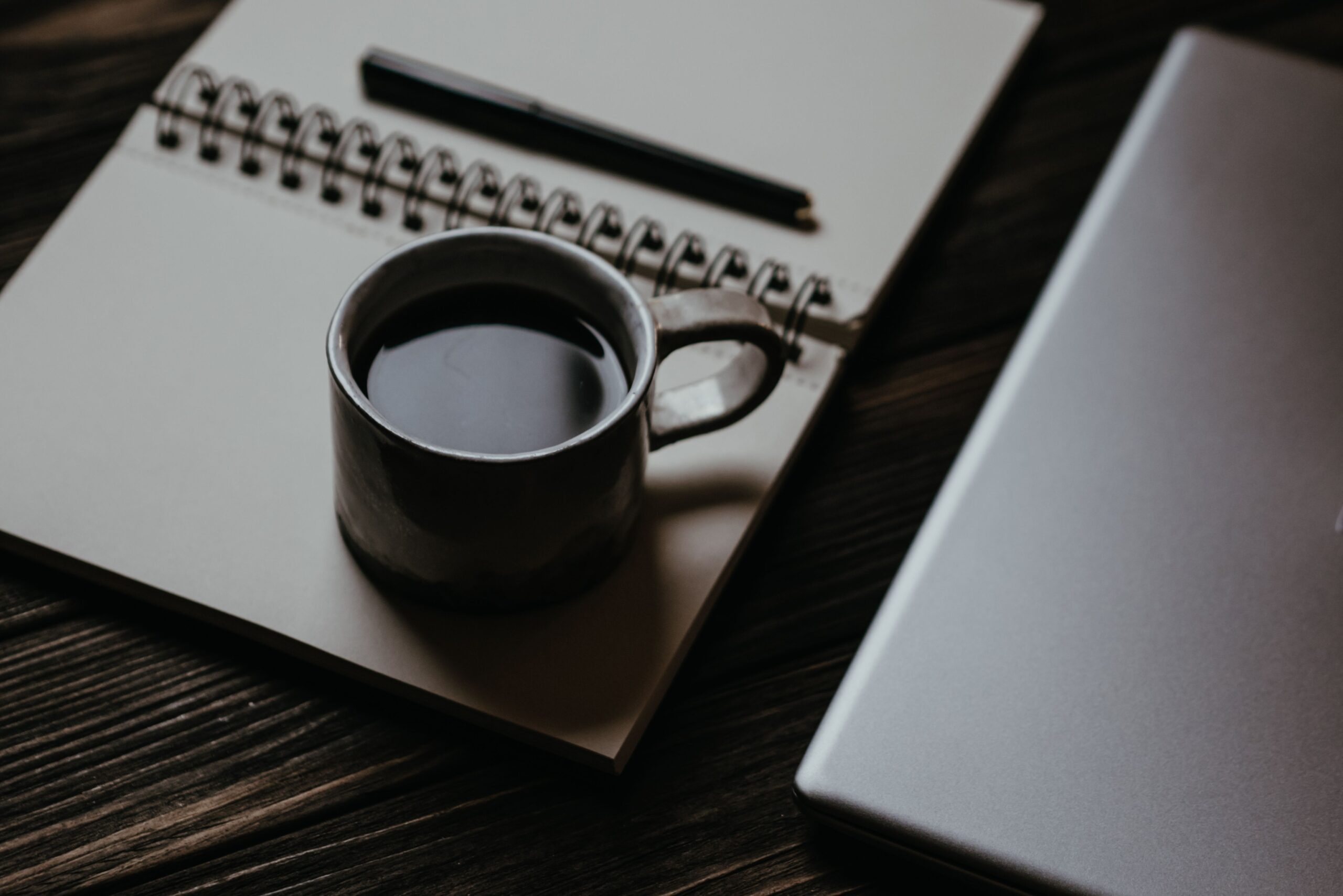 Arbeitsplatz mit Kaffeetasse, aufgeschlagenem Notizbuch und Laptop für die Planung eines Inhalts