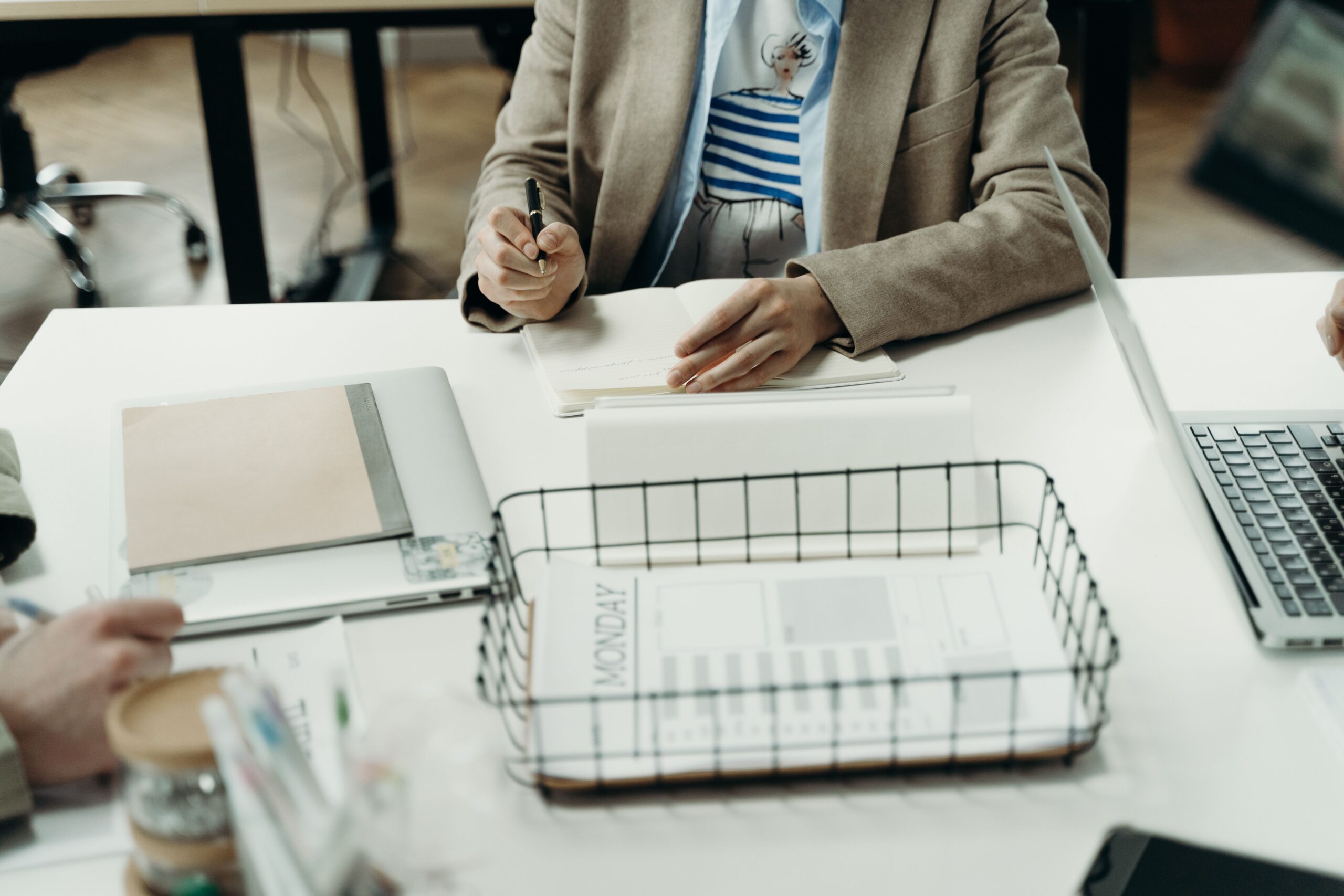 Person im Blazer macht sich mit einem Stift Notizen für eine Planung am Schreibtisch