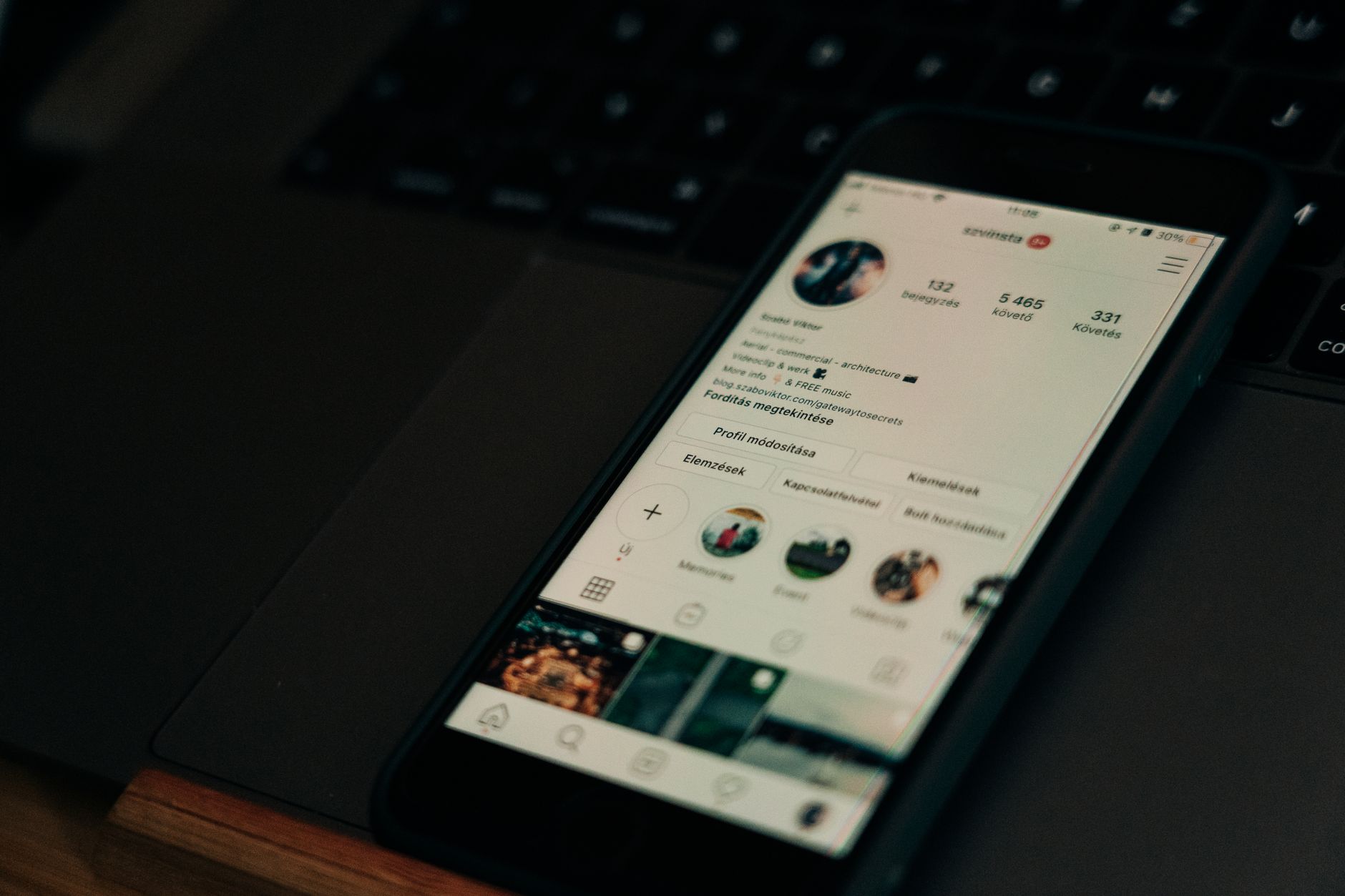 Smartphone mit geöffnetem Social-Media-Profil liegt neben einem Laptop auf dem Schreibtisch