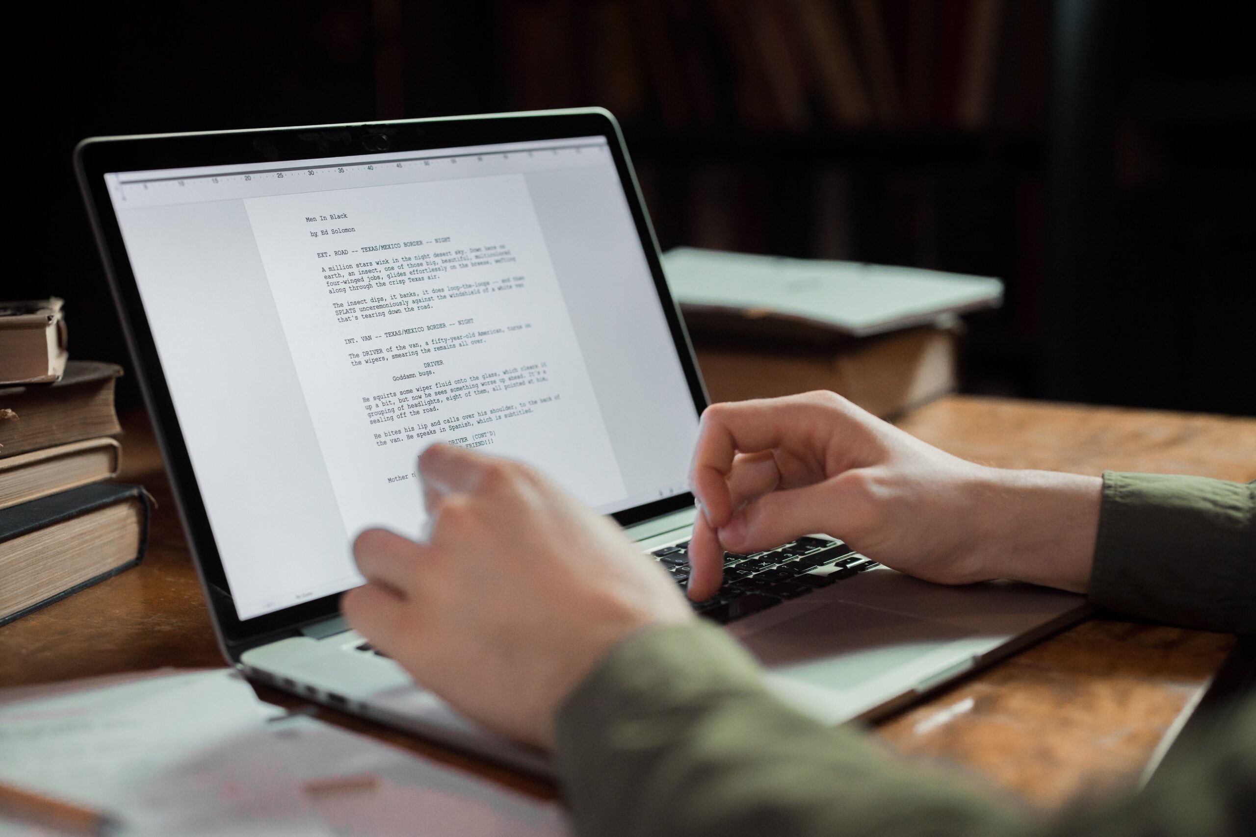 Person schreibt an einem Laptop, umgeben von Büchern auf dem Arbeitstisch
